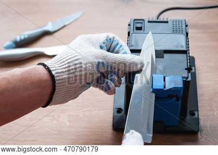 Sharpening A Knife On An Electric Sharpener At Home. The Man\'s Hand Drives The Knife Blade Between 