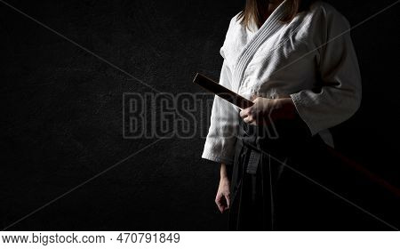 A Woman In Black Hakama Standing In Fighting Pose With Wooden Sword Bokken Over Grunge Dark Backgrou