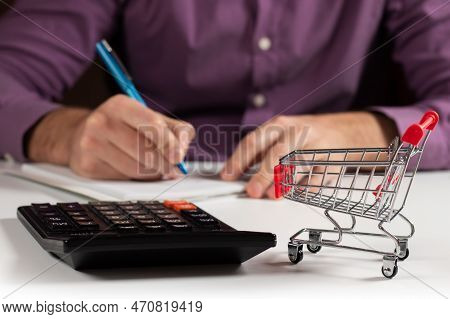 Man Calculates The Budget. Shopping Cart A On Table With Calculator And Paper. Budget Of Poor And Lo