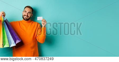 Happy Aduly Man Showing Credit Card And Shopping Bags, Standing Against Turquoise Background