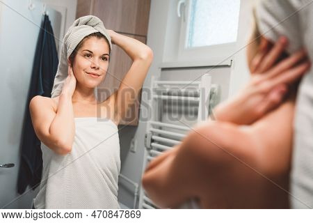 Young Caucasian Woman Looking At Herself In The Mirror With Her Hair Wrapped In A White Towl