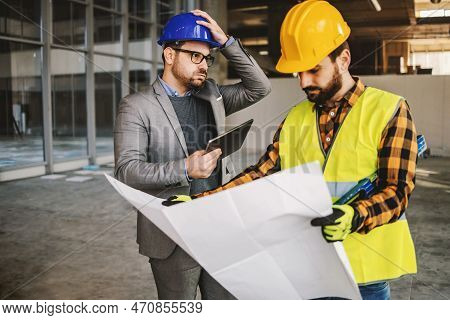 Supervisor Getting Upset About Works. Construction Site Worker Holding Blue Prints And Looking At It