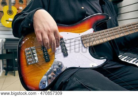 Demonstration Of A Bass Guitar In A Music Store. Close-up Of A Man's Hand Playing The Bass Guitar