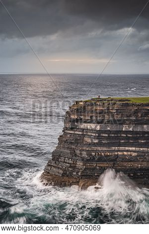 Fisherman Standing On The Edge Of Tall Downpatrick Head Cliffs With Crashing Waves Beneath At Dawn. 