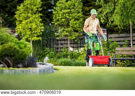 Professional Caucasian Gardener Spreading Seeds On The Lawn Using Garden Spreader Tool. Gardening Th