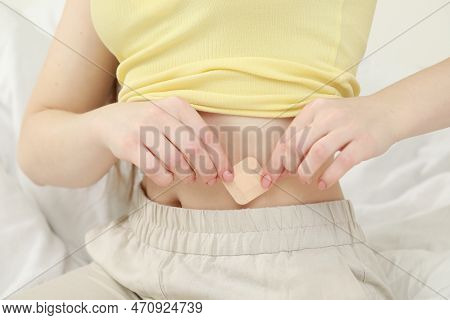 Woman Applying Contraceptive Patch Onto Her Belly On Bed, Closeup