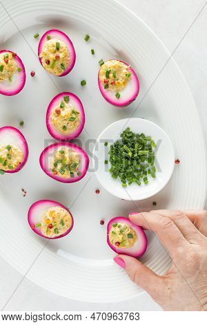 Hand Holding A Bright Pink Devilled Egg On A Platter With Several Devilled Eggs.