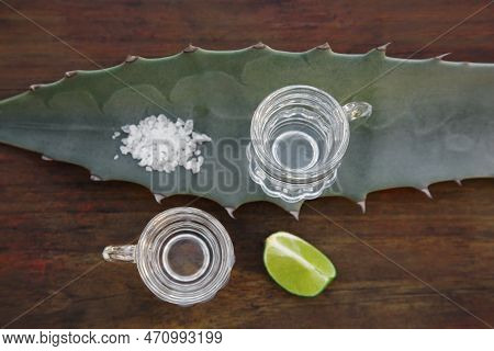 Mexican Tequila Shots, Salt, Lime Slice And Green Leaf On Wooden Table, Flat Lay. Drink Made Of Agav