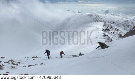 Climbers With Small Backpacks And Trekking Poles Are Walking On A Snowy Slope. Walk Above The Clouds