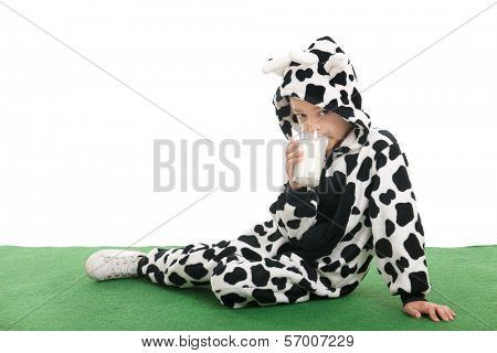 Little boy dressed as cow sitting in the grass and drinking milk