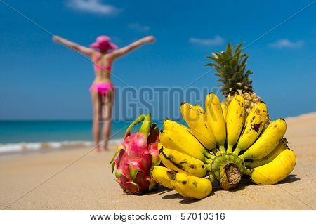 Tropical fruits and a woman in a bikini sunbathing on the beach on sea background. Idealistic scene