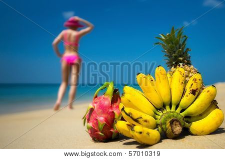 Tropical fruits and a woman in a bikini sunbathing on the beach on sea background. Idealistic scene