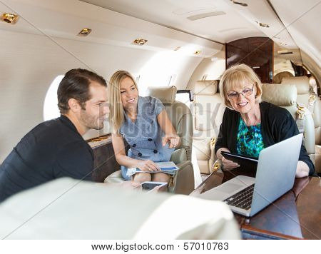 Businesswoman pointing at laptop to colleagues while discussing in private jet