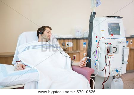 Young male patient listening to music while receiving renal dialysis in hospital room