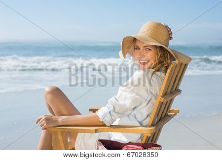 Smiling blonde sitting on wooden deck chair by the sea on a sunny day