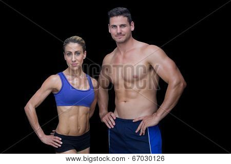 Crossfit couple smiling at camera with hands on hips on black background