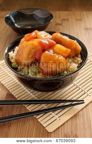 Sweet and sour chicken Cantonese style with egg fried rice in a lacquer bowl with chopsticks