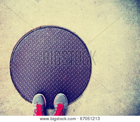 a pair of feet on a manhole cover done with a retro vintage instagram filter