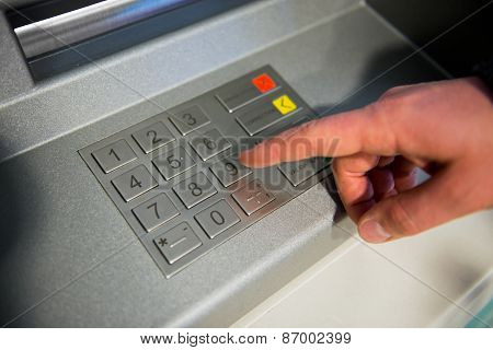 Close-up of hand entering PIN code on ATM machine keypad.