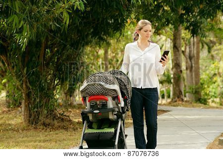 Mother With Baby In Pushchair Typing Message On Phone