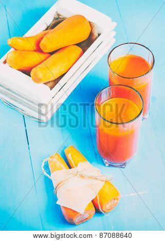 Freshly squeezed carrot juice in the glasses.A box with purified carrot on a blue wooden background.