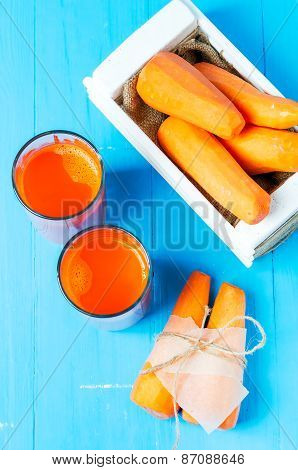 Freshly squeezed carrot juice in the glasses.A box with purified carrot on a blue wooden background.