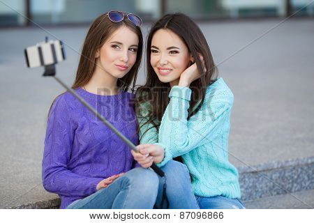 Two young attractive women are photographed with a smartphone on the streets.