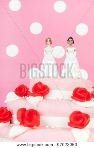 Pink wedding cake with red roses and lesbian couple on top