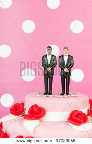 Pink wedding cake with red roses and gay couple on top