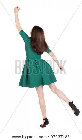 back view of writing beautiful woman. Young girl in dress. Rear view people collection.  backside view of person. The girl in stylish green dress standing on tiptoes writes a felt-tip pen on top. 