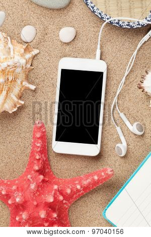 Smartphone on sea sand with starfish and shells. Top view with copy space