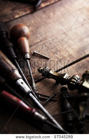 Old and well used screw driver with antique brass drawer handle in background. Antique restoration. Shallow depth of field. Low key.  