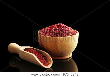 Sumac in wooden bowl, isolated on black