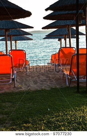 Beachscape with orange chairs, thatched sunshades and island in a background