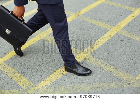 Legs of businessman with briefcase walking down trottoire