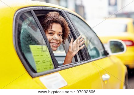 business trip, transportation, travel, gesture and people concept - young smiling african american woman driving in taxi and waving hand at city street