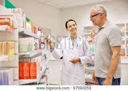 medicine, pharmaceutics, health care and people concept - happy pharmacist showing drug to senior man customer at drugstore