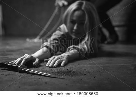 Not helpless anymore. Anxious stubborn young woman reaching a dagger lying near her making an tempt escaping