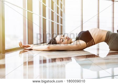 Young Woman Practice Yoga Matsyasana Against Windows In Studio.