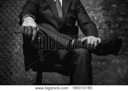 If you still have doubts. Powerful stylish dangerous criminal striking a power pose while wearing classy suit and holding a gun in his hand