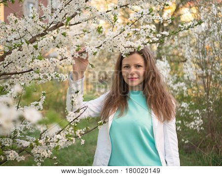 outdoor portrait of a beautiful woman in white jacket among white blossom tree.