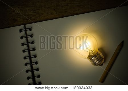 A Light Bulb With A Small Pencil Placed On An Opened Sketchbook