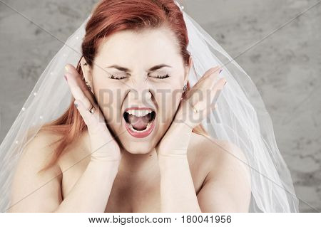 Funny red haired bride is screaming with hands up. Isolated on grey background. 