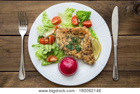 served Homemade Breaded Schnitzel with salad and berry sauce on old wooden table