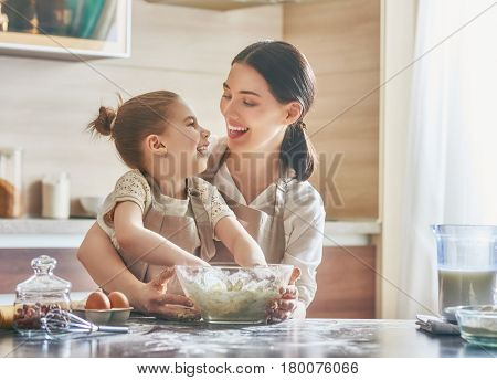 Happy loving family are preparing bakery together. Mother and child daughter girl are cooking cookies and having fun in the kitchen. Homemade food and little helper.