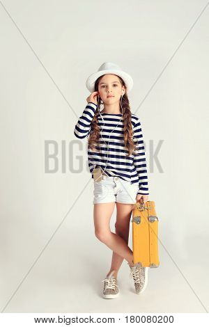 Young nice girl is holding yellow suitcase and listening to music through earphones on smartphone. Travel, tourism, vacation, listening music concept