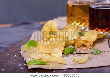 Potato chips with salt and greens on a table in a pub on a background of beer. Chips with greens as a snack to beer. October Beer Fest.