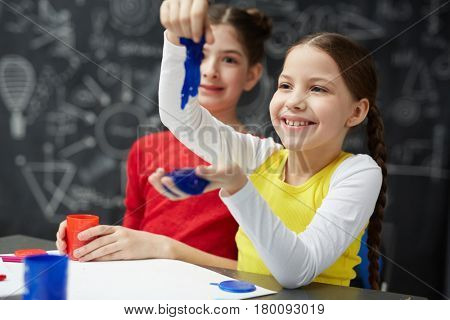 Smiling girl playing with blue slime in school