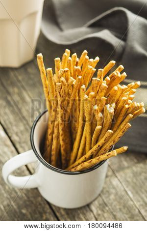 Salty pretzel sticks in white cup.