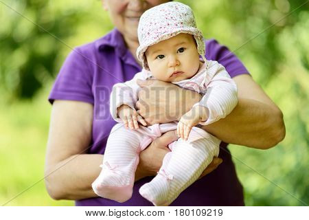 Baby girl on the hands of her grandmother in nature